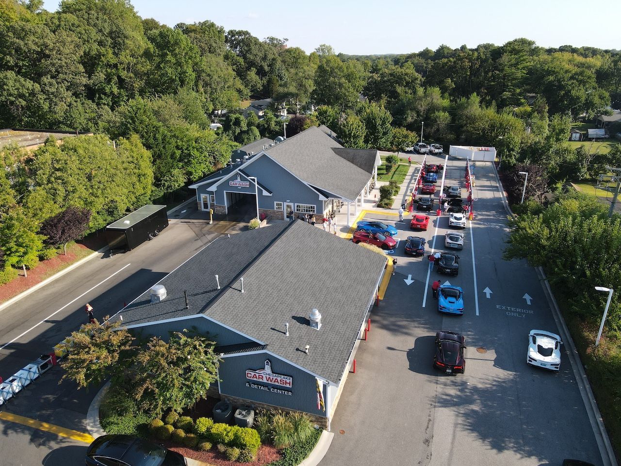 Aerial view of a parking lot beside a dark-roofed building, with many cars and trees around it