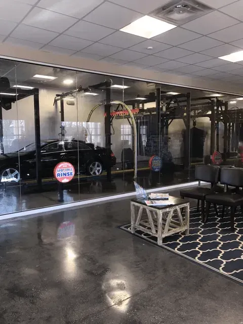 Interior view of a car wash with a black car and waiting area with chairs, a table, and a rug.