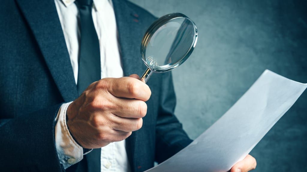 Man in suit examines document with magnifying glass.