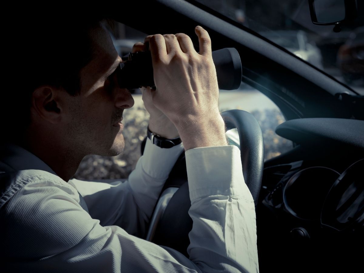 Man in car looking through binoculars.