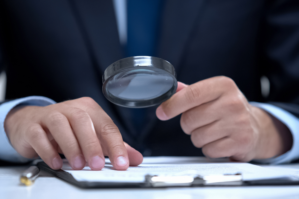 Person in a suit examining a document with a magnifying glass.