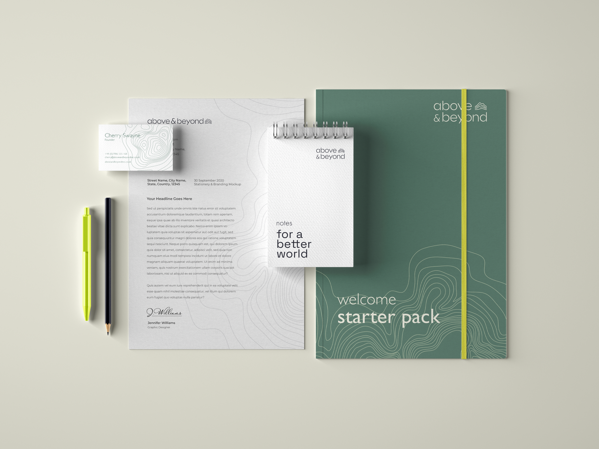 Stationery branded with the above and beyond logo and company colours (cream, sage green and navy) is laid out, evenly spaced, with a pen, pencil, business card, notepad and large note book. .