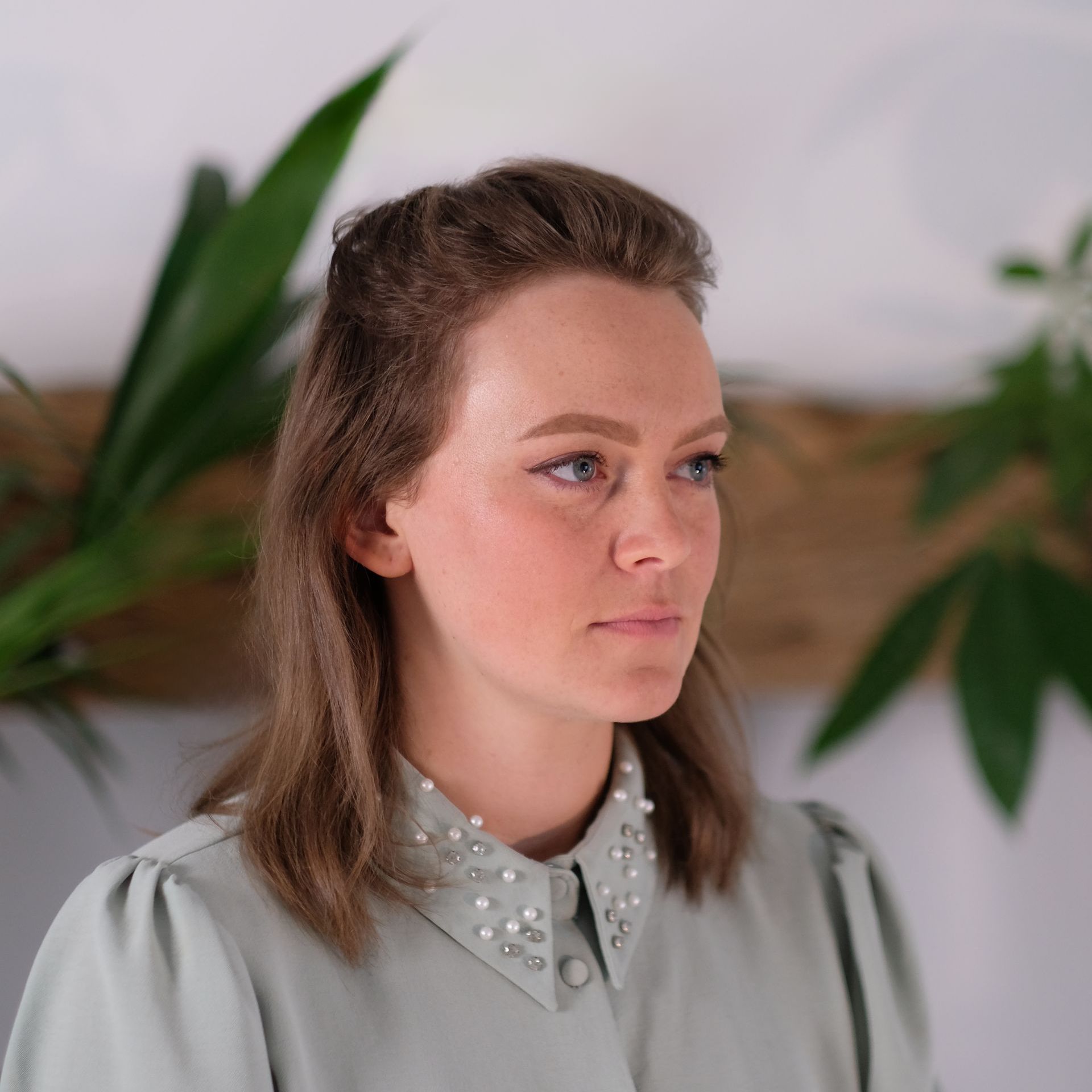 Headshot: a white woman with light brown hair looks into the distance wearing a blue-grey top with embellished collar