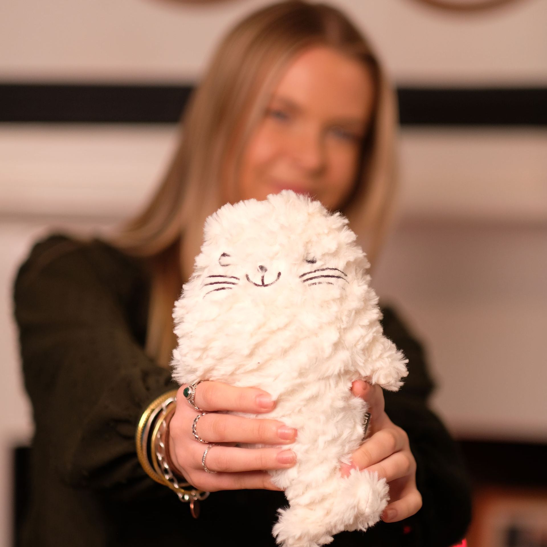 Headshot:  a young white woman with blond hair is blurred out in the background as she holds up a fluffy white toy seal..