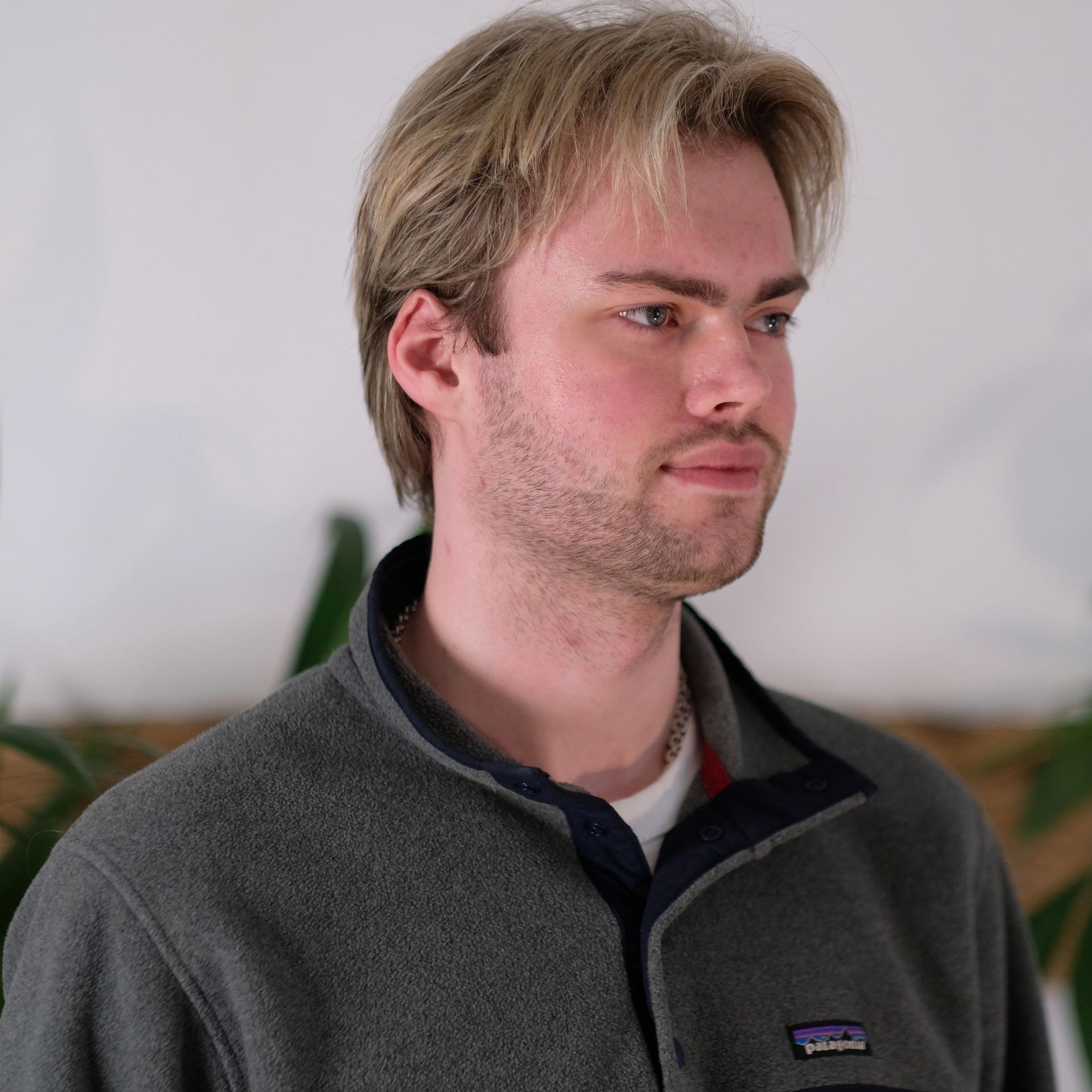 Headshot: a white man with blond hair and stubble looks to the side of the camera wearing a fleece with a zip