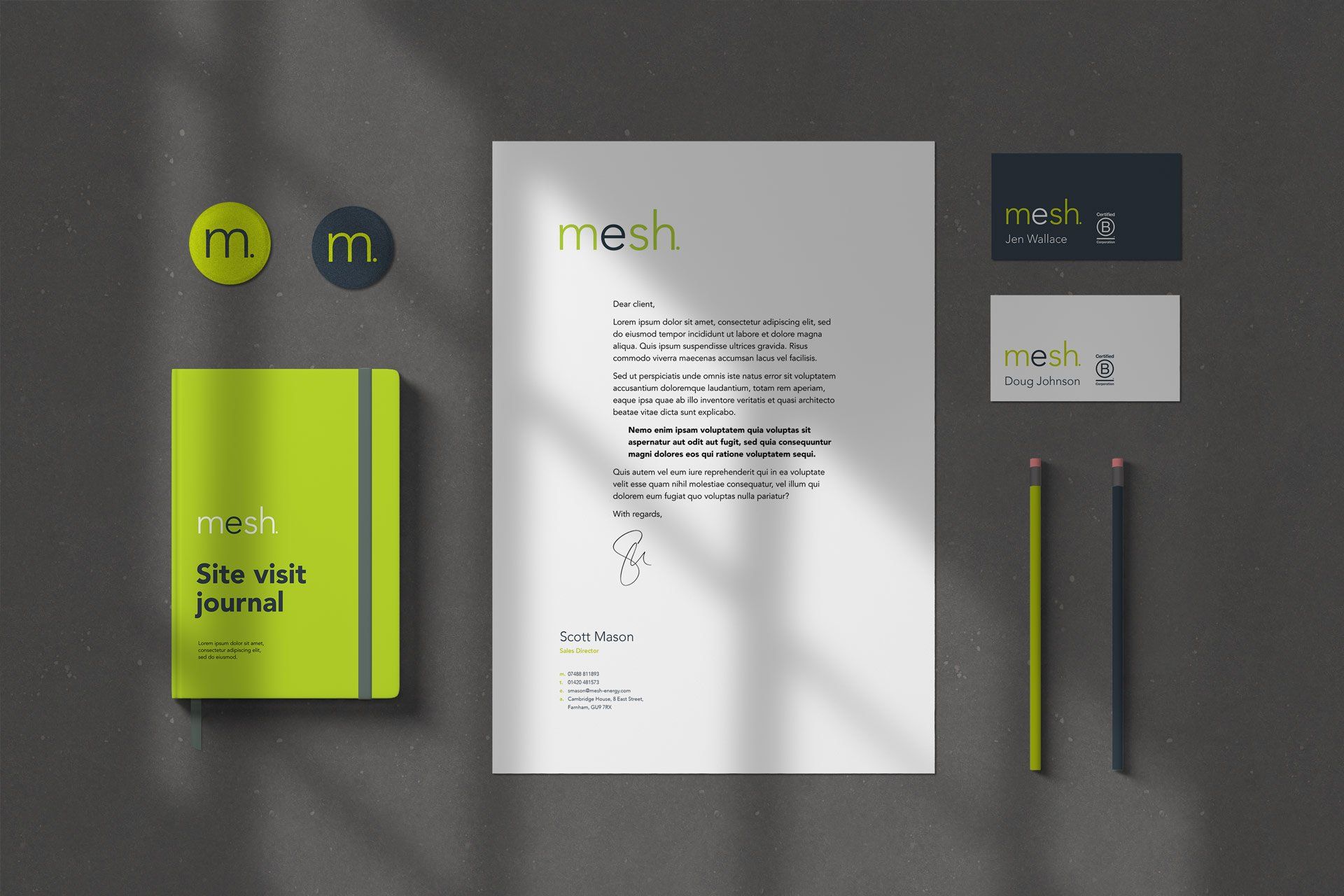 Stationary branded with the mesh logo and company colours (white, navy blue, and lime green) is laid out, evenly spaced, and a grey table.