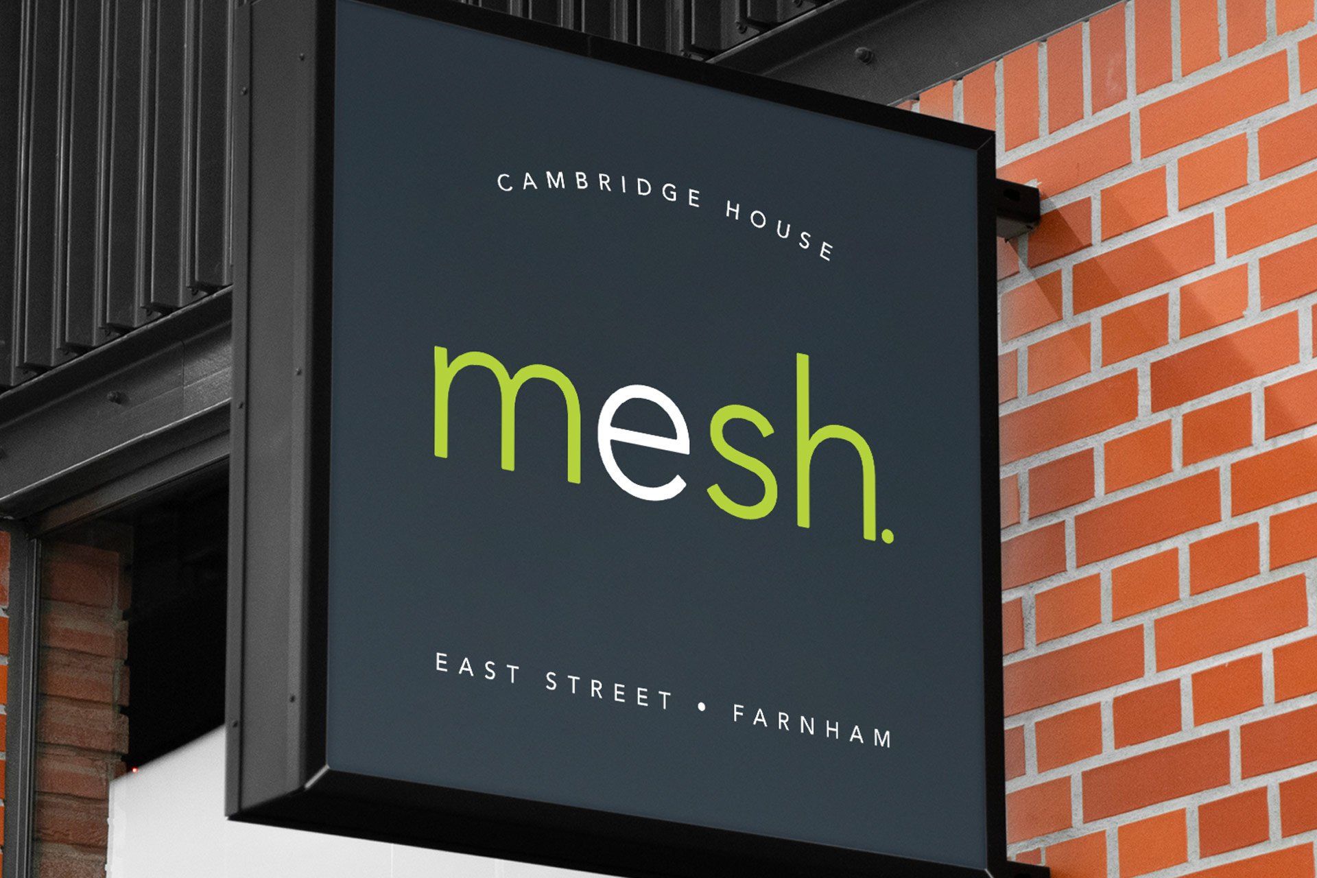 The mesh logo shown on a sign protruding from a red brick wall. The sign also reads 