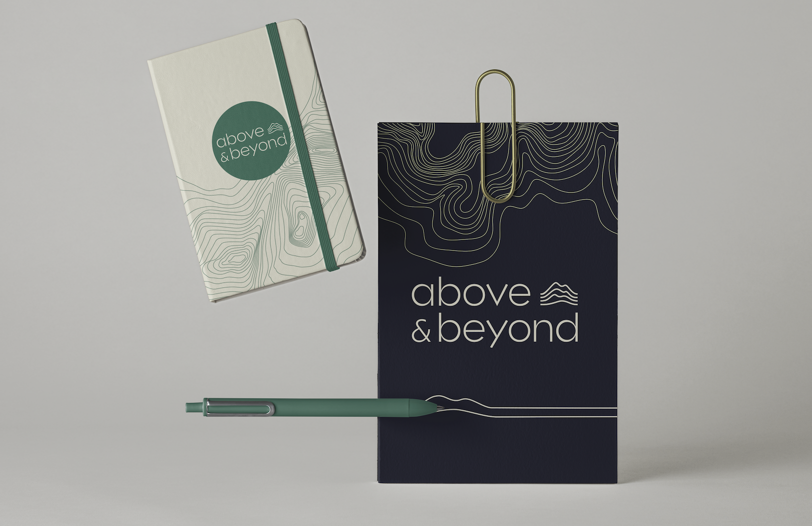 A cream and green branded notebook, with a navy and cream branded card and large gold paperclip and green pen.