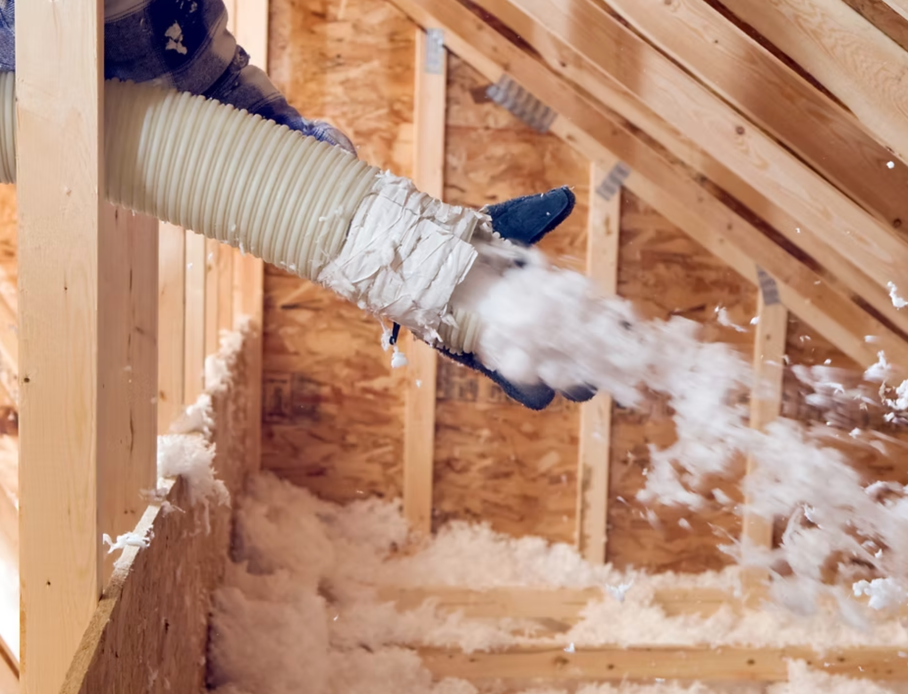 A person is blowing insulation into the attic of a house.