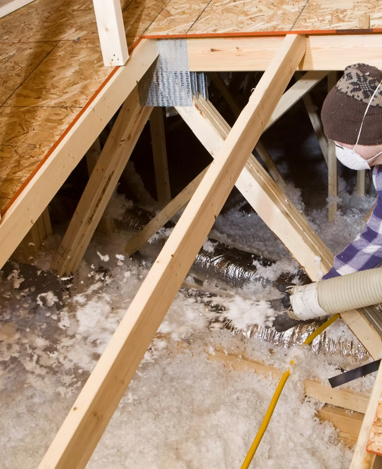 A man wearing a mask is blowing insulation into an attic
