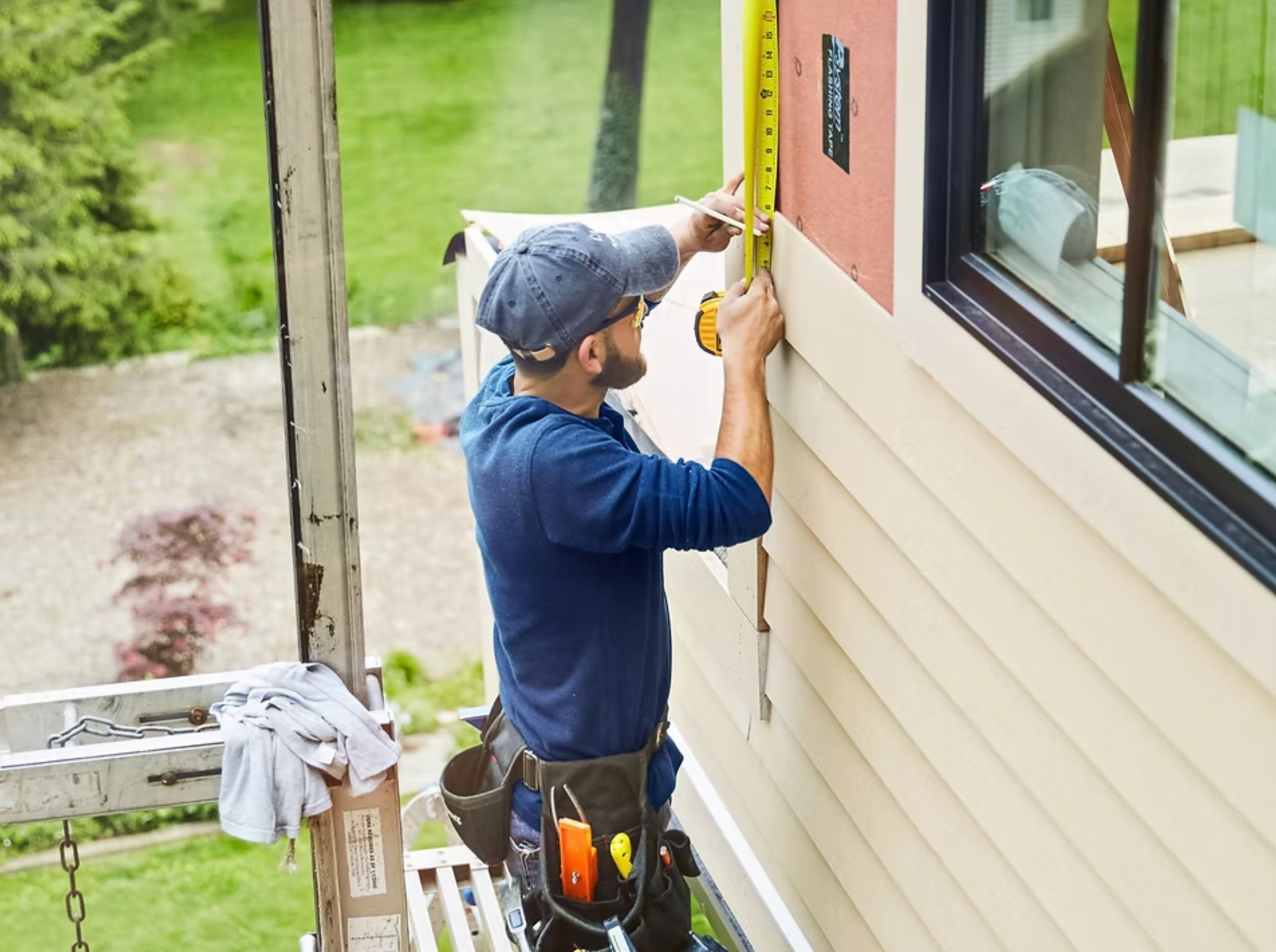 A man is measuring the side of a house with a tape measure.