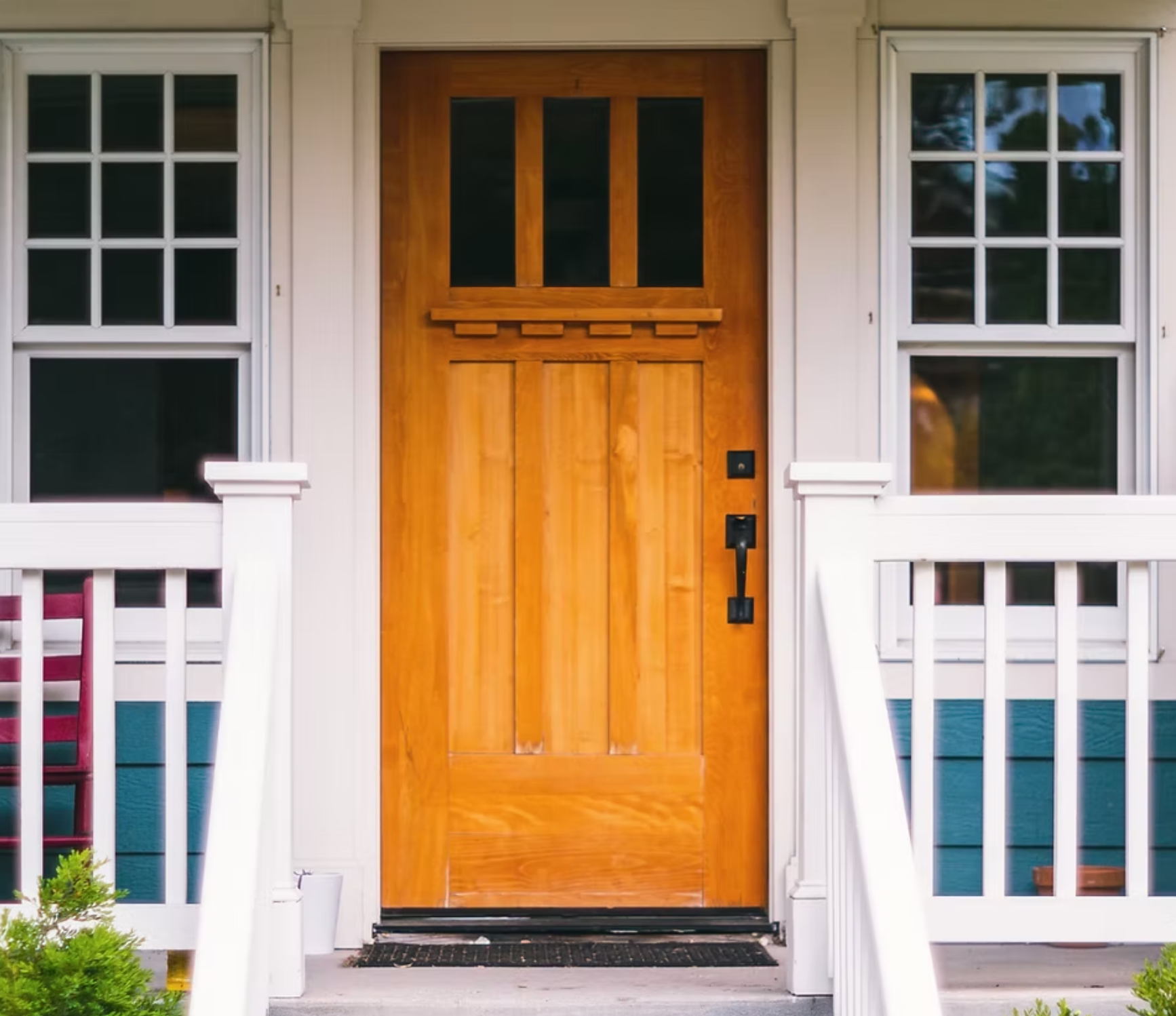 The front door of a house with a wooden door and a white railing.