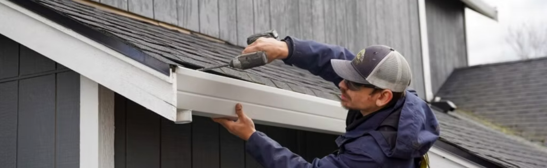 A man is working on the roof of a house with a drill.