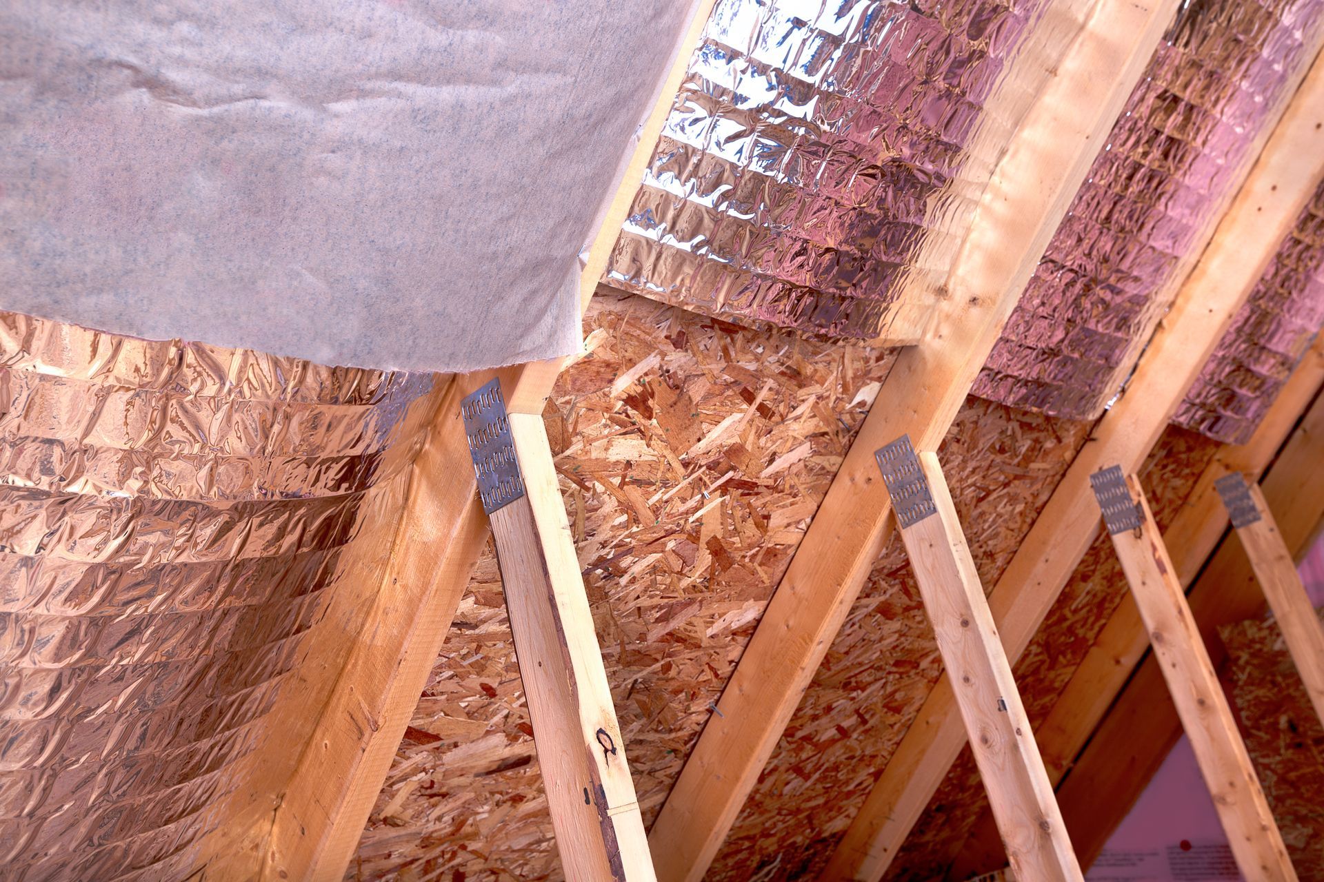 Wooden rafters with reflective foil insulation in an attic.