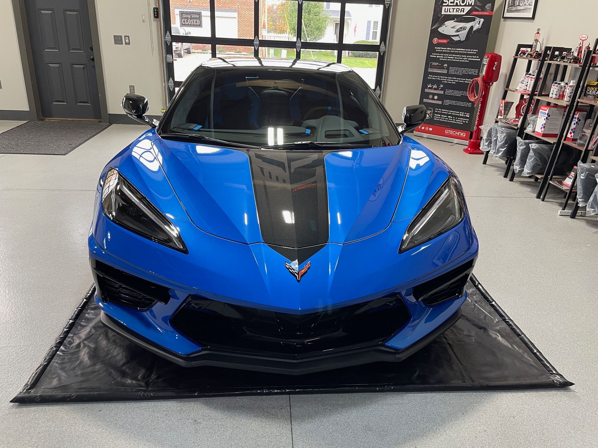 Blue sports car with black racing stripe parked on black mat in garage.