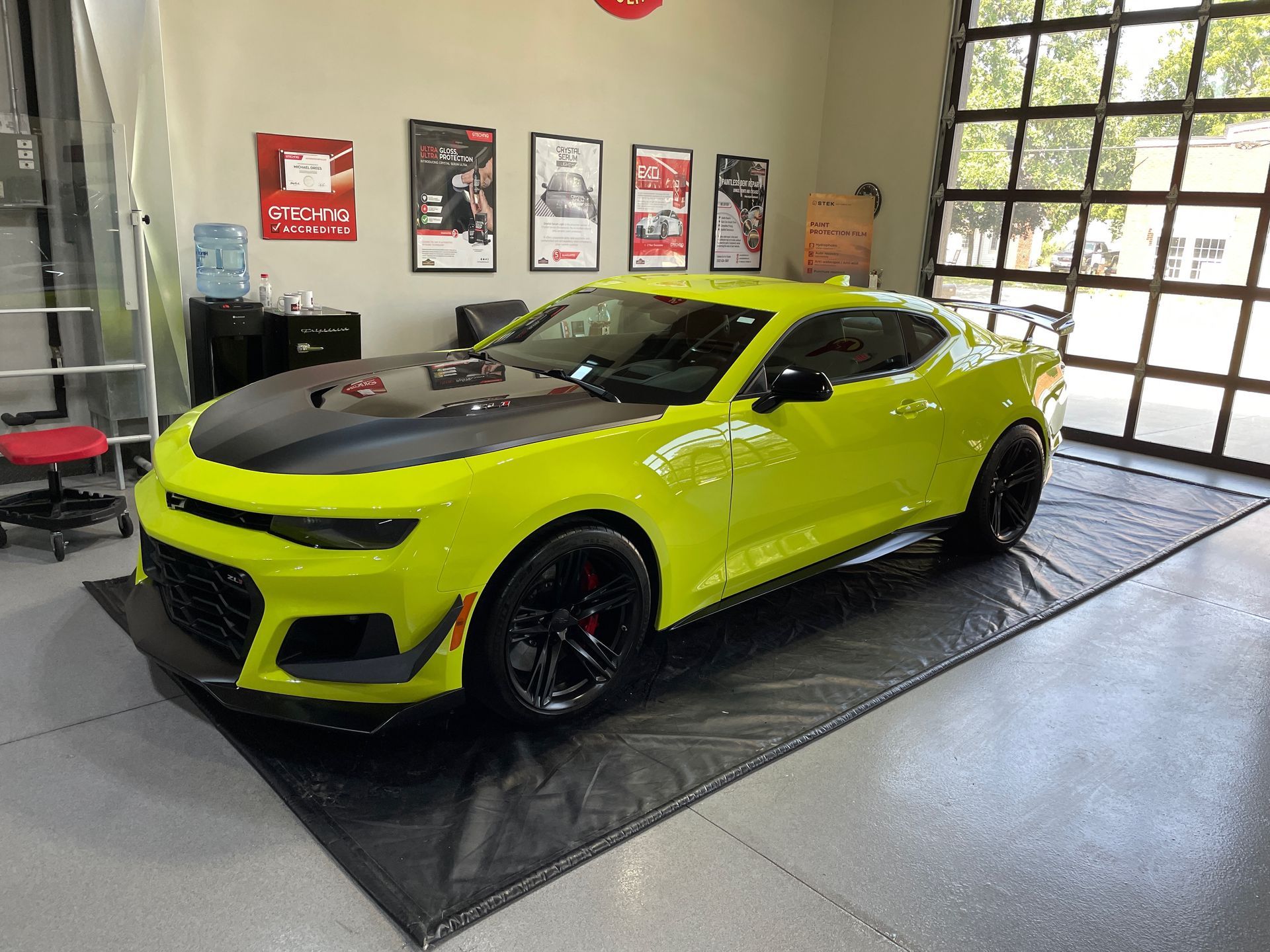 Bright yellow Camaro with black hood and wheels, parked inside a garage.