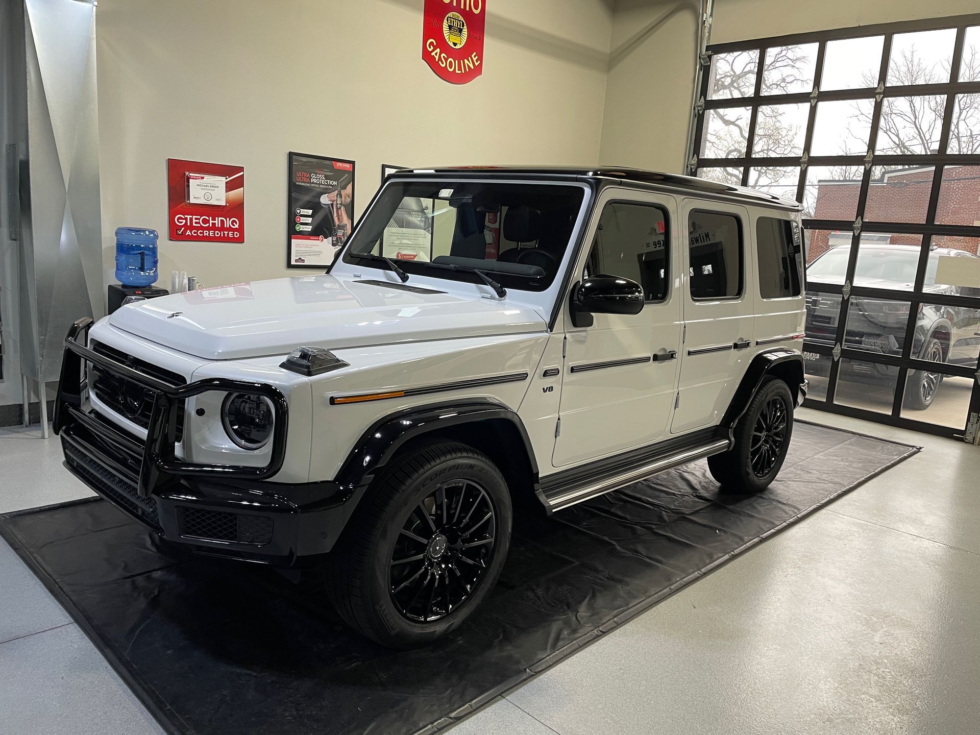 White Mercedes-Benz G-Wagon SUV with black accents parked on a mat inside a showroom.