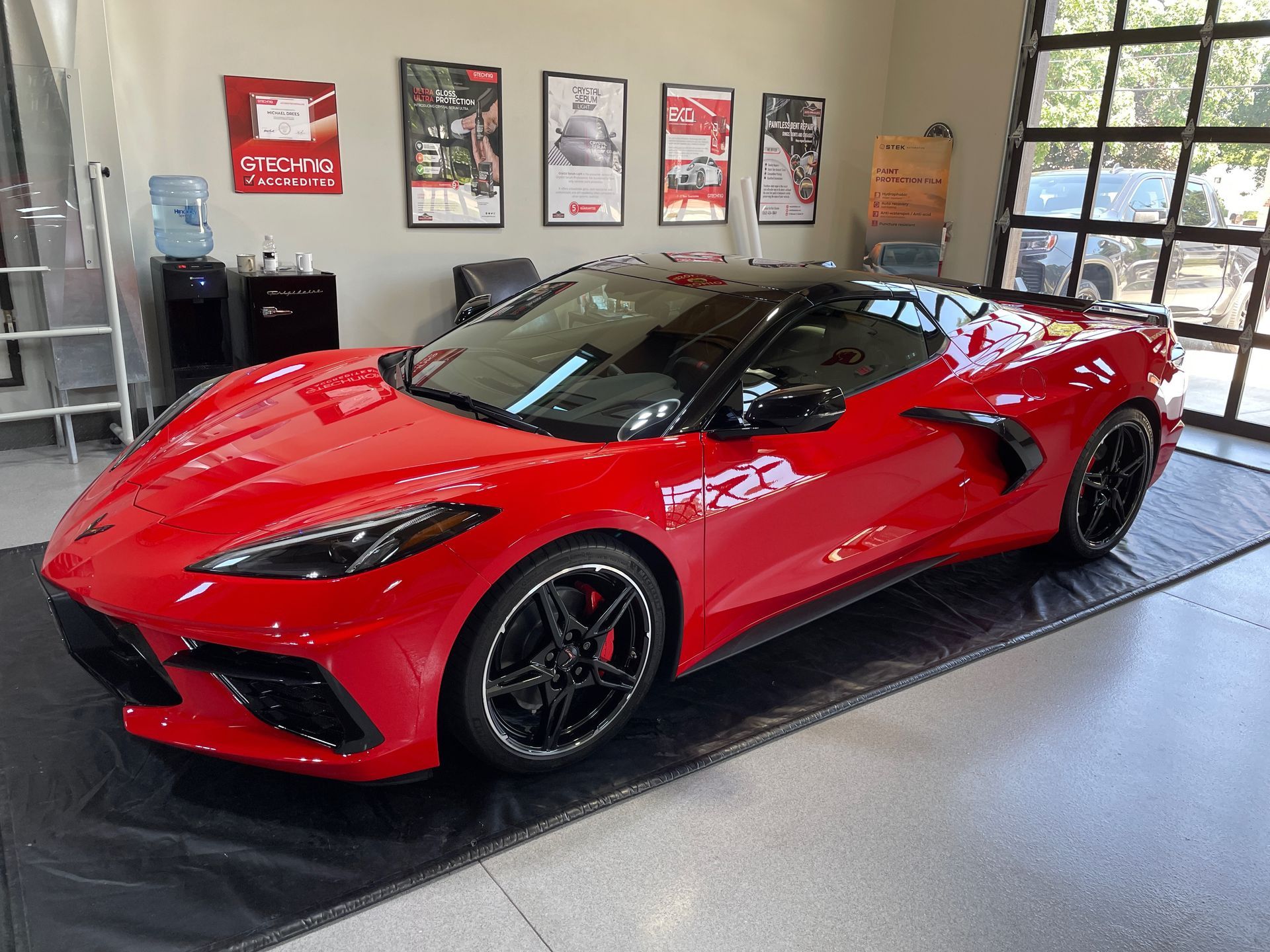 Red Corvette with black roof and wheels in a showroom.