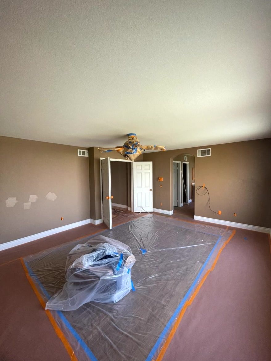 Room under renovation with brown walls, white trim, ceiling fan, and plastic covering furniture.