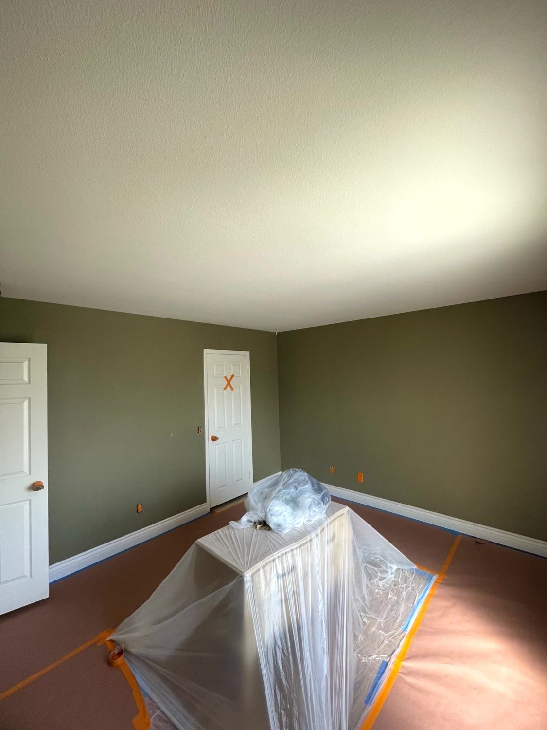 Empty room with green walls, white ceiling and trim. A covered object sits in the center.
