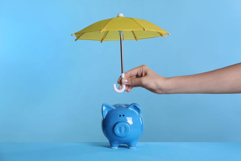 Protecting income — hand holding umbrella over blue piggy bank (Ovation Tax Group concept)