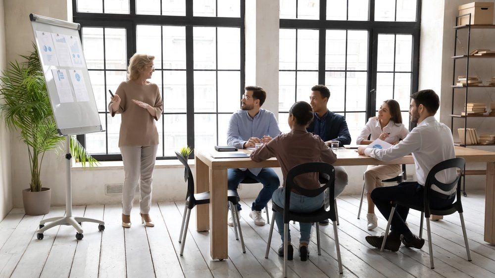 A woman is giving a presentation to a group of people sitting around a table.