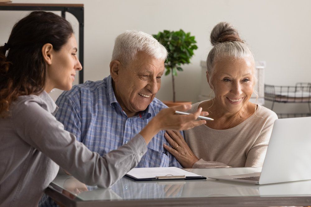 An elderly couple is sitting at a table looking at a laptop.