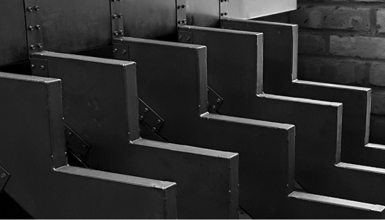 Black and white close-up of zigzag metal staircase against a brick wall.
