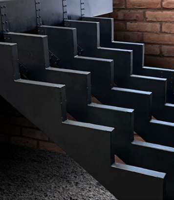 Dark metal zig-zag staircase against a brick wall.