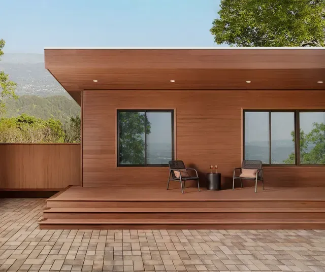 Wood-paneled modern building with deck, two chairs, and forest view.