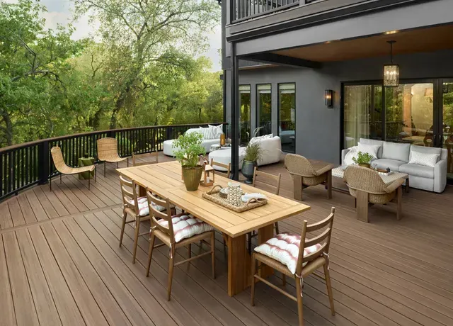 Wooden deck with outdoor dining table and seating, overlooking a green, wooded area.