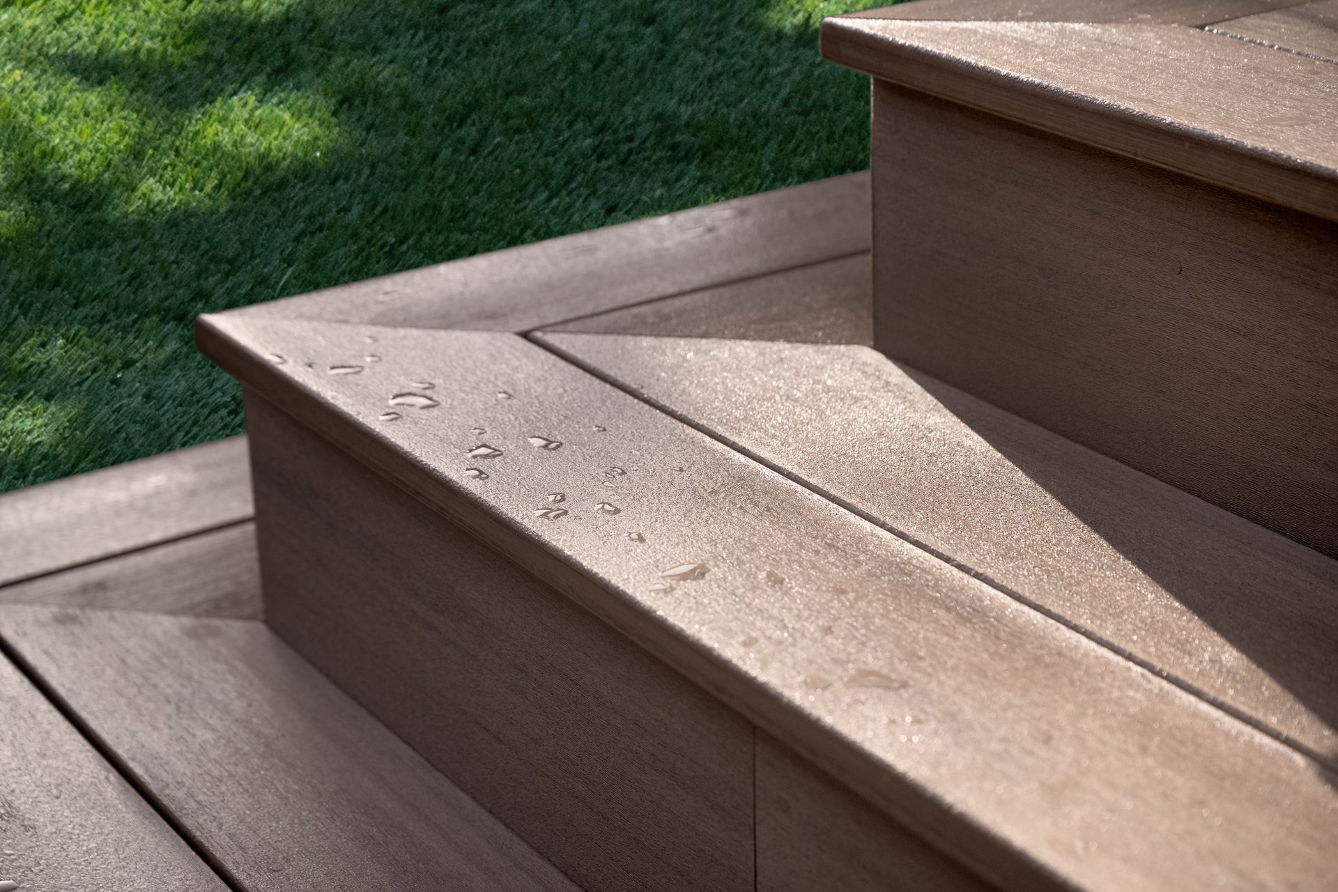 Brown composite deck stairs with water droplets, green grass in the background.