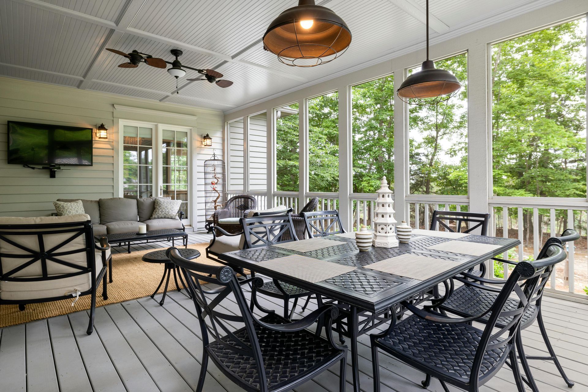 Covered porch with dining table and seating, view of trees, and a mounted TV.