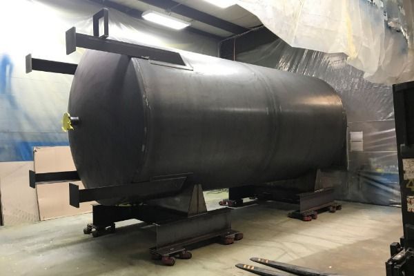 A large black tank is sitting in a room with a forklift.
