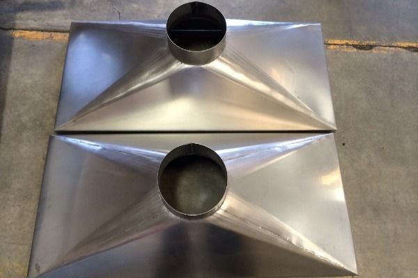 Two stainless steel plates with holes in them are sitting on a concrete floor.