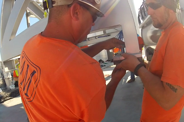 Two men in orange shirts are working on a piece of equipment.