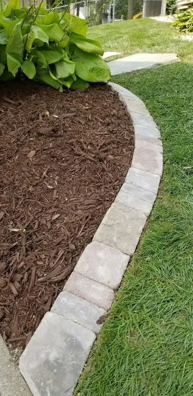 Curved stone garden border edging brown mulch and green lawn beside leafy shrubs