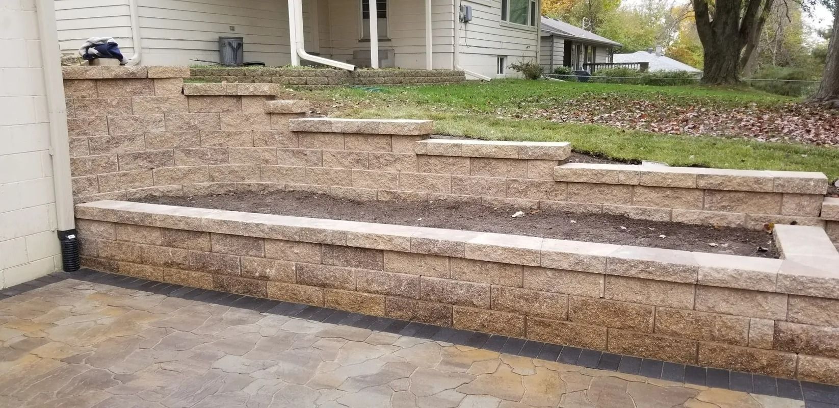 Stone retaining wall steps leading up a sloped gravel yard beside a house and tree