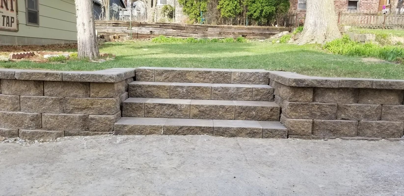 Stone steps built into a low retaining wall beside a paved path in a park-like setting