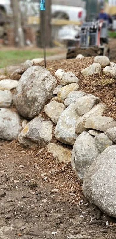 Stone retaining wall along a dirt path, lined with large and small white rocks.
