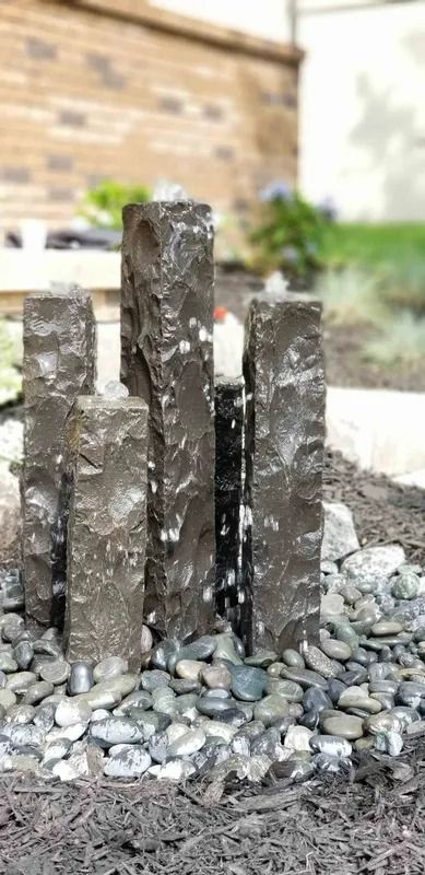 Three dark wooden posts in wet gravel near a brick wall outdoors