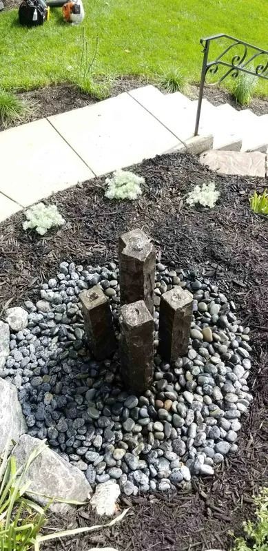 Small garden water feature with dark wooden posts, gray stones, and a stone path beside green grass