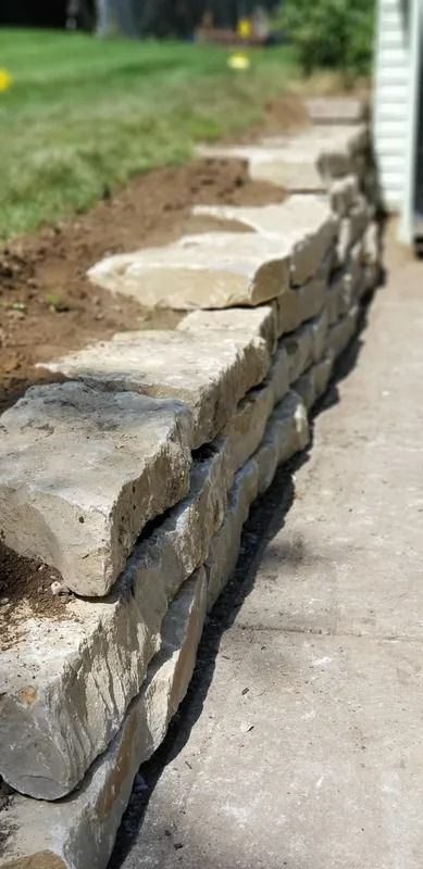 Low stone garden retaining wall beside a concrete walkway and grass lawn