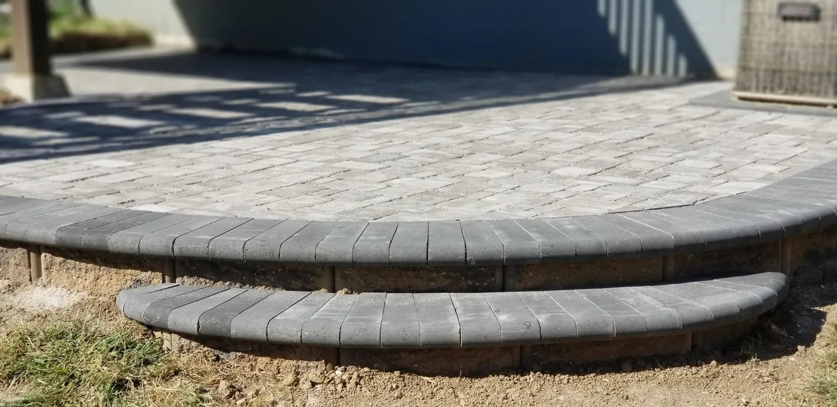 Curved stone patio step with a low front ledge beside a grassy yard and building wall