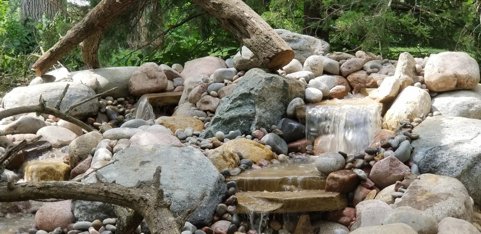 Rocky streambed with a small waterfall beneath an arched tree branch and stacked stones