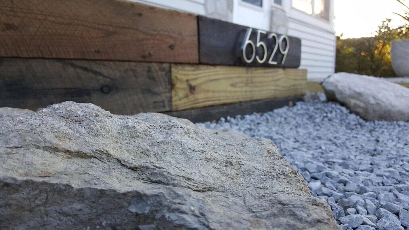 House number 6529 on a wooden exterior beside rocks and gravel landscaping