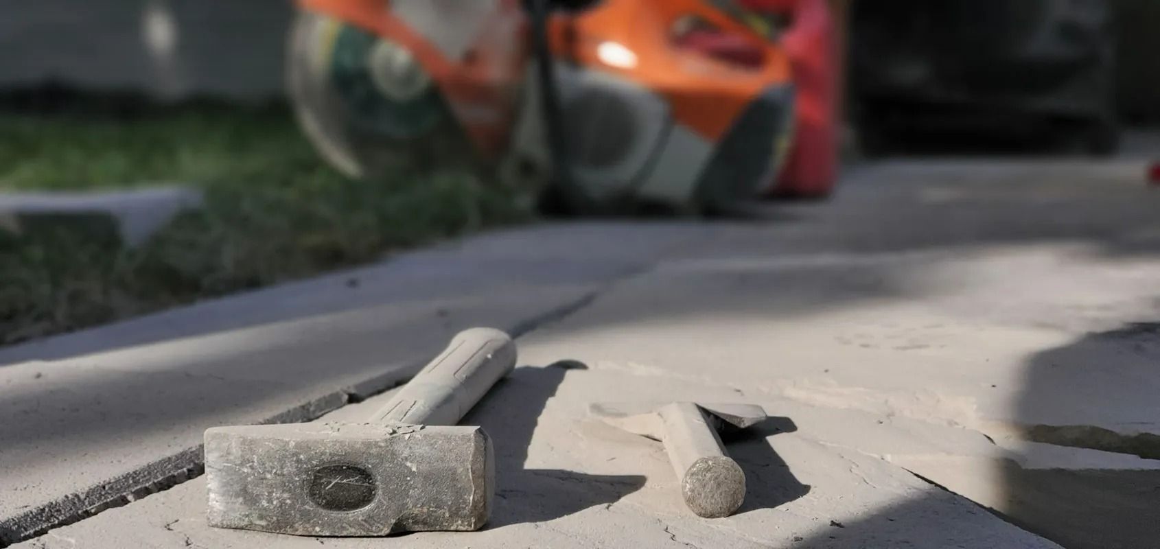Broken concrete pieces on a sunlit sidewalk with a blurred orange bicycle in the background