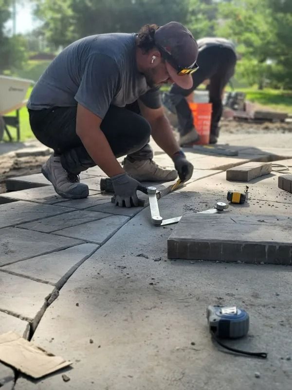 Worker kneeling on a patio, measuring stone pavers with a tape measure during installation