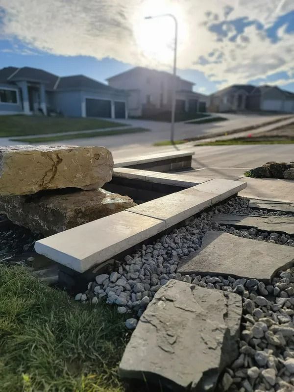 Damaged sidewalk slab propped over rocks beside a suburban street at sunrise