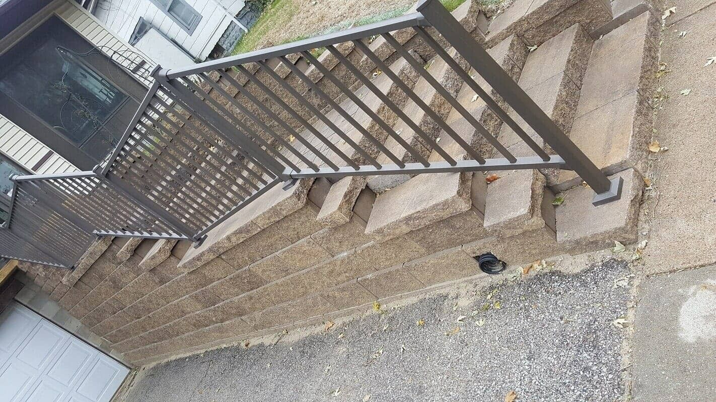Tilted outdoor staircase with black metal railing beside a gravel path and house wall